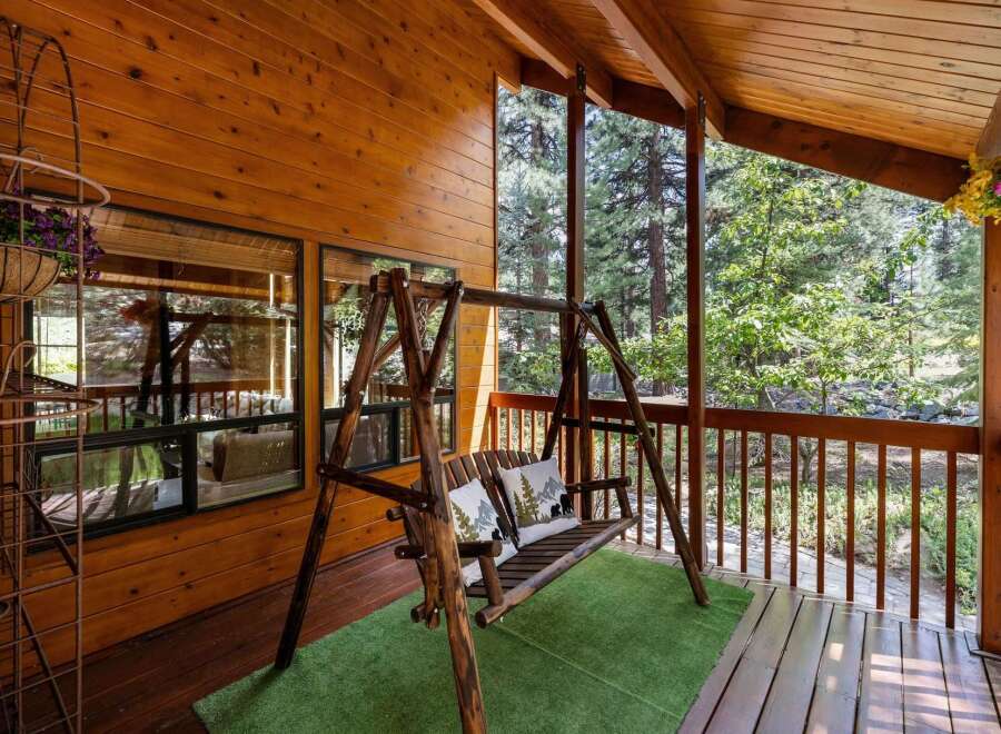 Enjoy the tranquility of this charming cabin porch, complete with a cozy swing and lush greenery.