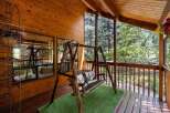 Enjoy the tranquility of this charming cabin porch, complete with a cozy swing and lush greenery.