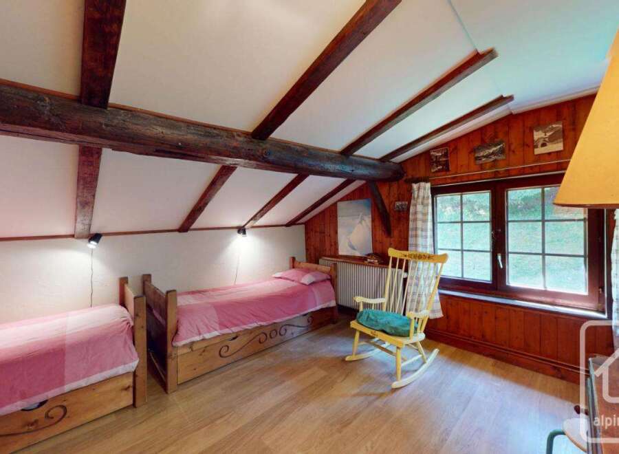 This charming bedroom features a cozy, rustic design with exposed wooden beams and a sloped ceiling, creating a warm and inviting atmosphere.