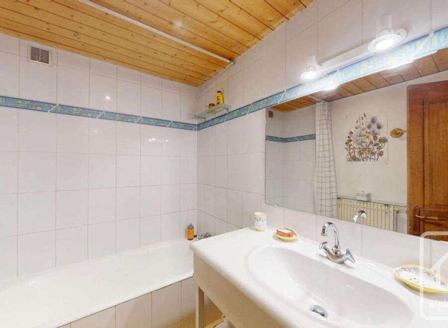 This charming bathroom features a classic design with white tiled walls and a wooden ceiling, creating a warm and inviting atmosphere.