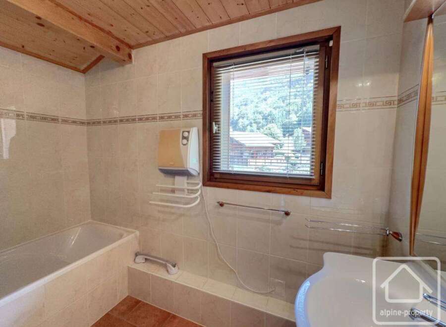This charming bathroom features a cozy ambiance with its wooden ceiling and tiled walls.
