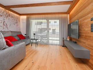 Experience the warmth and elegance of this stunning living space, featuring beautiful wooden floors and a cozy gray sofa with vibrant red pillows.
