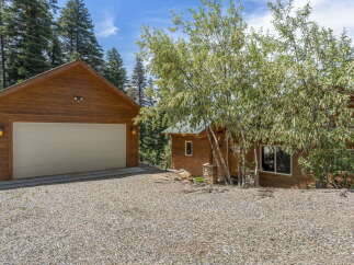 Nestled in a serene natural setting, this property boasts a charming wooden exterior and a spacious gravel driveway.