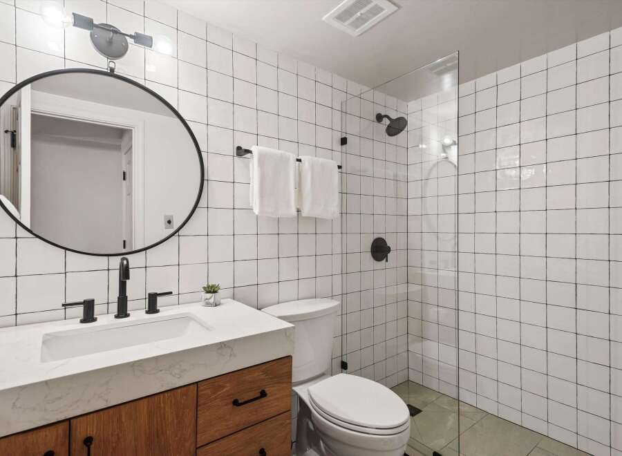 This modern bathroom features a sleek design with white square tiles and black accents.