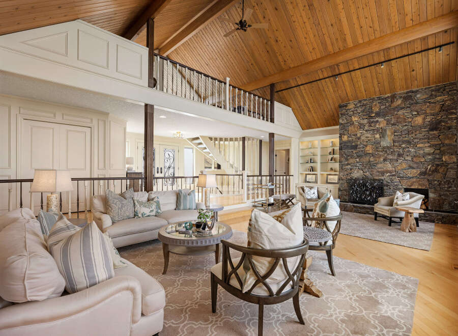 This stunning living room boasts a grand, open design with a soaring wood-paneled ceiling and a cozy stone fireplace.