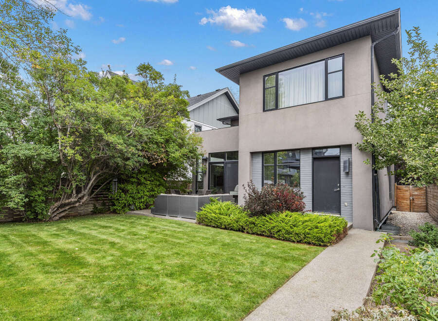 This stunning modern home boasts a beautifully manicured lawn and lush landscaping, creating an inviting outdoor space.