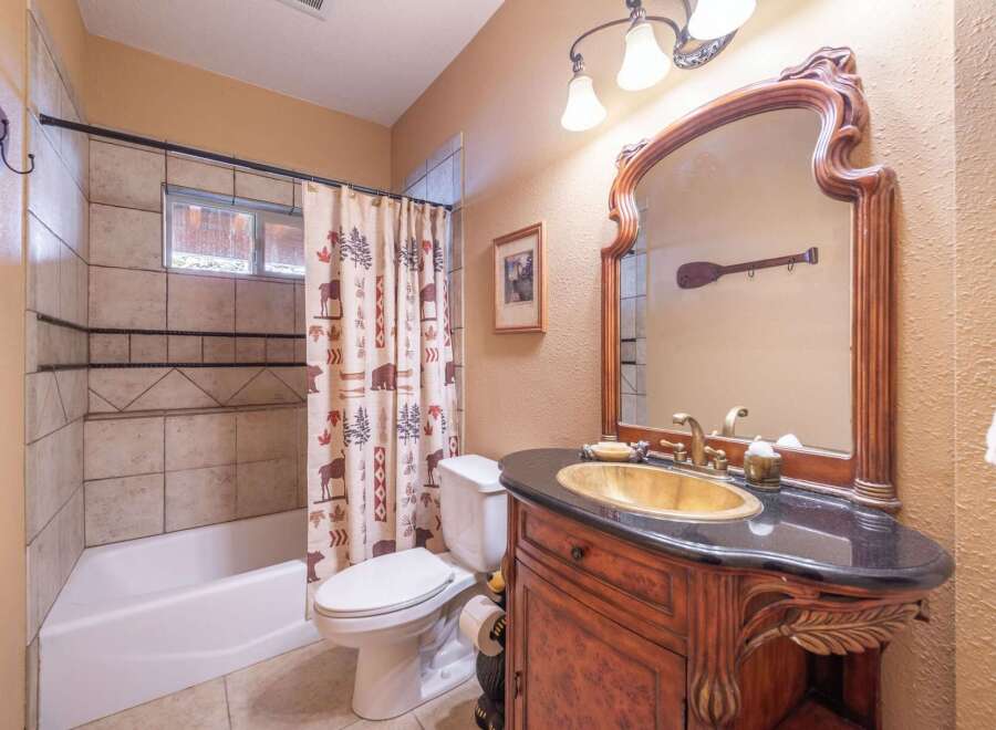 Step into this charming bathroom, featuring a rustic vanity with a unique gold sink and a stylish black countertop.