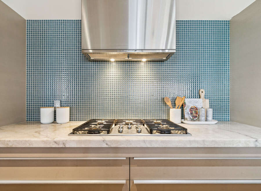 This stunning kitchen features a sleek stainless steel range hood, complemented by a beautiful blue tile backsplash.