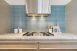 This stunning kitchen features a sleek stainless steel range hood, complemented by a beautiful blue tile backsplash.