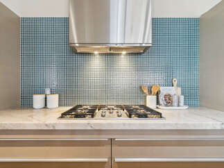 This stunning kitchen features a sleek stainless steel range hood, complemented by a beautiful blue tile backsplash.