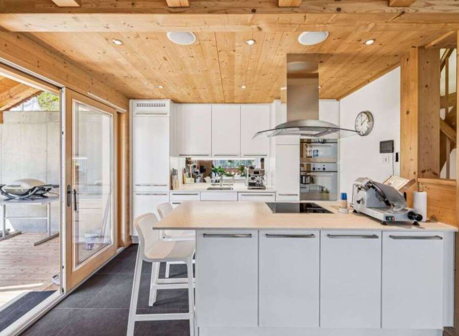 This stunning kitchen boasts a modern design with a touch of rustic charm, featuring a beautiful wooden ceiling and sleek white cabinetry.