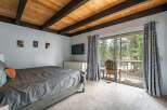 This stunning bedroom boasts a rustic charm with its wooden ceiling beams and a serene view of the surrounding nature.