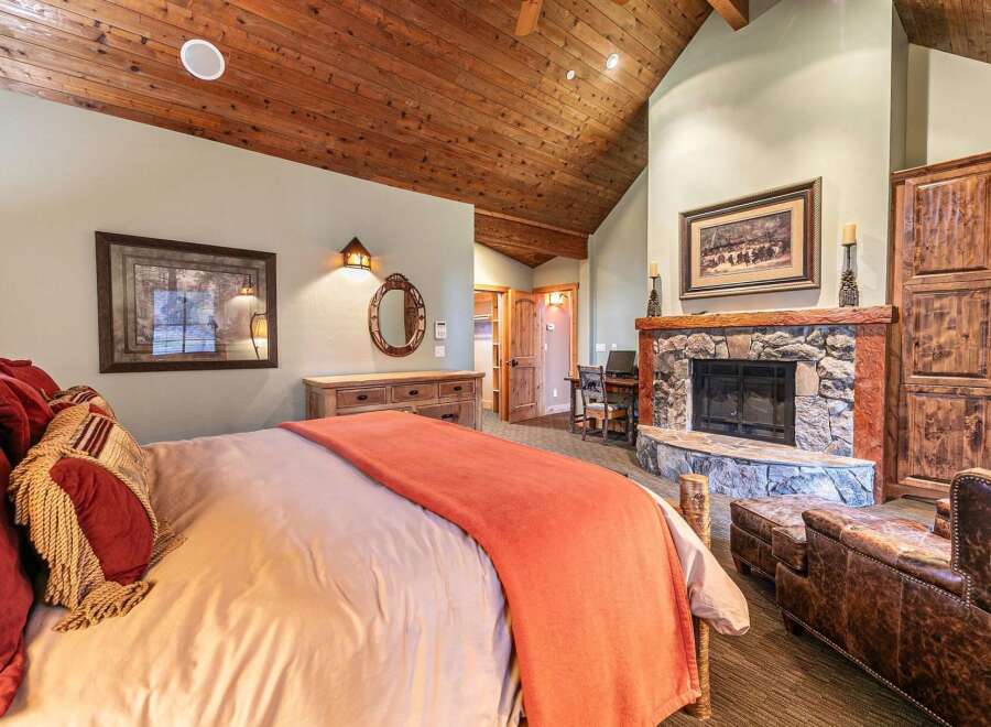 Experience rustic luxury in this stunning bedroom featuring a cozy fireplace and a vaulted, wood-paneled ceiling.