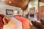 Experience rustic luxury in this stunning bedroom featuring a cozy fireplace and a vaulted, wood-paneled ceiling.