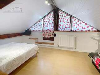 This charming attic bedroom features a cozy bed and a unique window design.