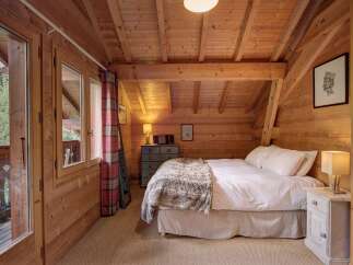 This charming bedroom features a cozy, rustic design with wooden walls and a sloped ceiling, creating a warm and inviting atmosphere.