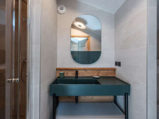This modern bathroom features a stylish teal sink and a sleek, oval-shaped mirror.