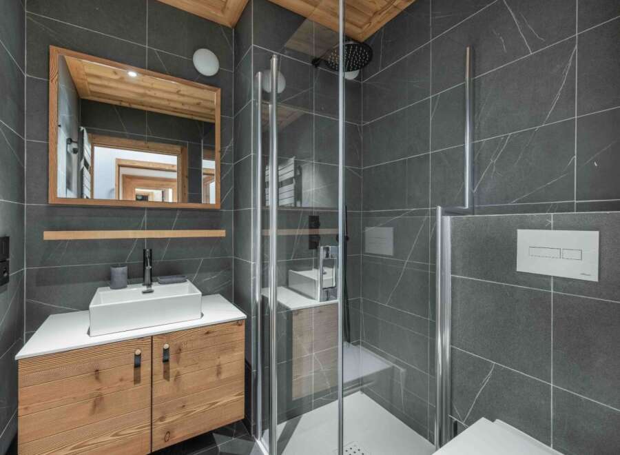 Step into a modern bathroom oasis, featuring sleek gray tile and a stylish wooden vanity.