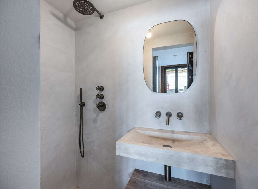 This modern bathroom features a sleek, minimalist design with a concrete sink and a unique, rounded mirror.
