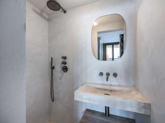 This modern bathroom features a sleek, minimalist design with a concrete sink and a unique, rounded mirror.