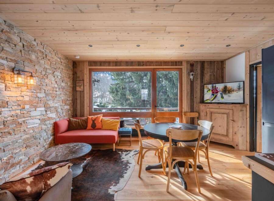 Experience the warmth of this stunning living space, featuring a rustic stone wall and a cozy red sofa, perfect for relaxing after a day on the slopes.