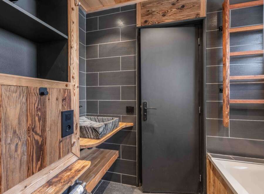 This stunning bathroom boasts a rustic design with wooden accents and dark gray tiles, creating a cozy and inviting atmosphere.