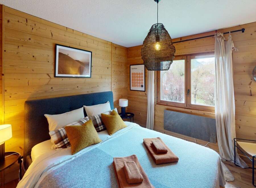 Discover the charm of this cozy bedroom, featuring warm wooden walls and a stylish pendant light.