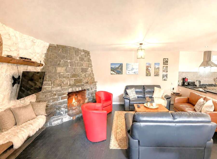Experience the warmth and charm of this stunning property, featuring a cozy living room with a stone fireplace and a mounted TV.