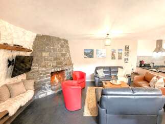 Experience the warmth and charm of this stunning property, featuring a cozy living room with a stone fireplace and a mounted TV.