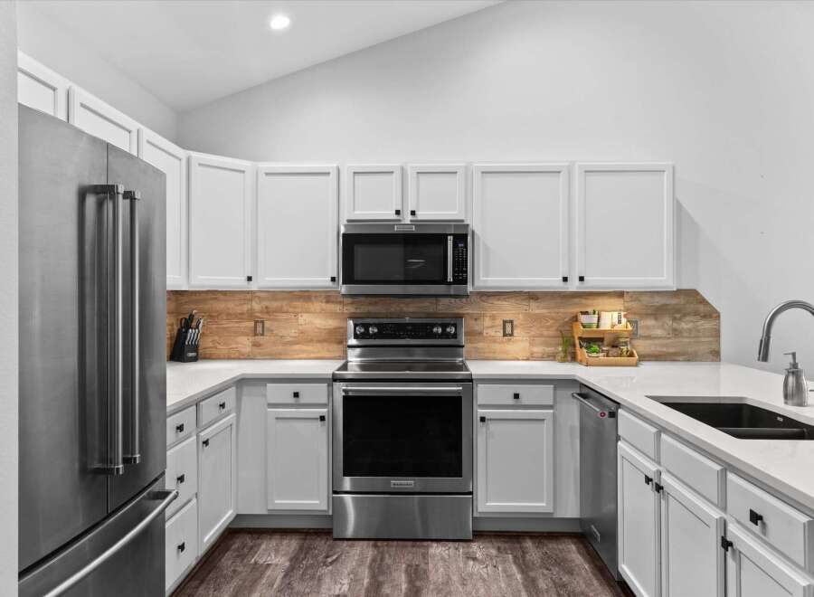 This modern kitchen features sleek white cabinetry, a stainless steel refrigerator, and a matching range with a built-in microwave.