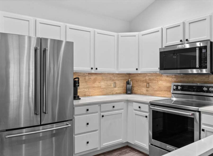 This modern kitchen features sleek stainless steel appliances, including a French door refrigerator and a matching range with a smooth cooktop.