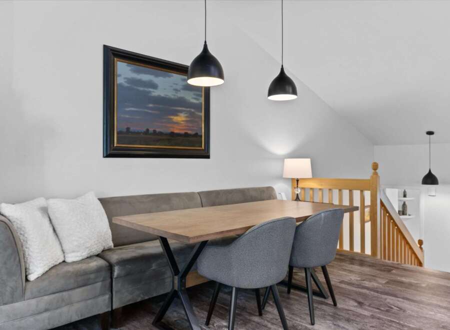 This dining area features a comfortable banquette with plush white pillows, complemented by a modern wooden table and two upholstered chairs.