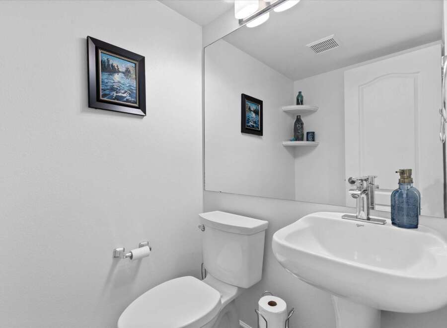 This charming powder room features a pristine white pedestal sink with a modern chrome faucet, complemented by a decorative blue soap dispenser.