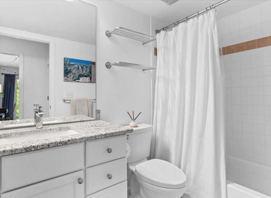 This bright and clean bathroom features a spacious vanity with a granite countertop and ample storage.