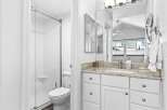 This bright and airy bathroom features a spacious walk-in shower with white tiled walls and a convenient corner shelf.