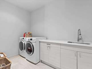 This modern laundry room features a sleek design with a washer and dryer set, a built-in sink, and ample counter space.