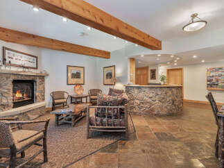 Step into the inviting warmth of this charming lodge-style living space, featuring a cozy stone fireplace and exposed wooden beams.