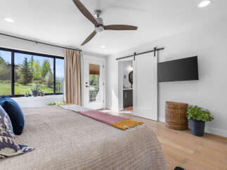 Step into a serene bedroom retreat, featuring a modern ceiling fan, a sleek mounted TV, and a stylish sliding barn door.
