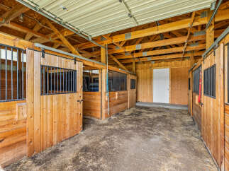Step into this inviting horse stable, featuring sturdy wooden stalls and a spacious layout.