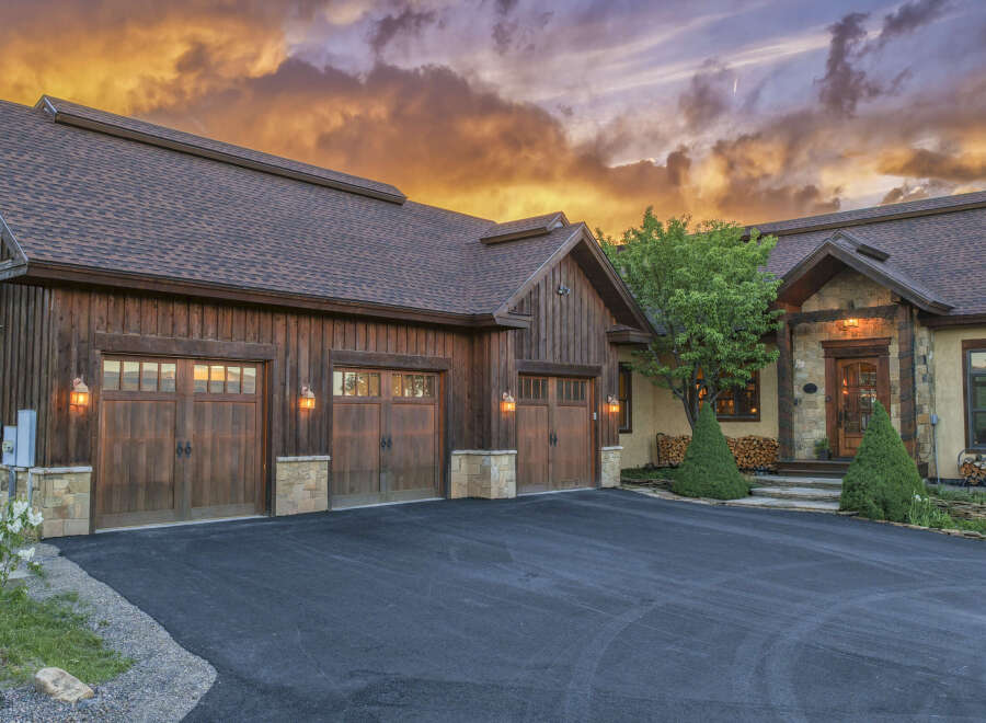 Experience luxury mountain living in this stunning timber-frame home, featuring a spacious four-car garage and a dramatic sunset sky.