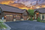Experience luxury mountain living in this stunning timber-frame home, featuring a spacious four-car garage and a dramatic sunset sky.