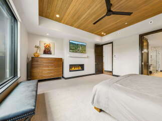 Experience luxury living in this stunning bedroom featuring a modern fireplace, a sleek TV, and a beautiful wooden ceiling.