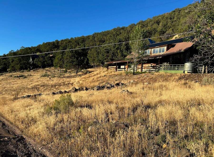 Nestled against a lush, tree-covered hillside, this rustic property offers a unique blend of natural beauty and functional design.