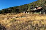 Nestled against a lush, tree-covered hillside, this rustic property offers a unique blend of natural beauty and functional design.