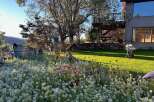 Discover a charming property with a lush garden blooming with white and pink flowers, leading to a rustic home featuring a multi-level deck perfect for outdoor entertaining.