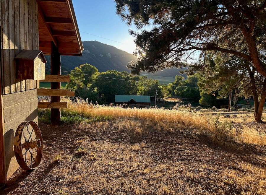 Experience rustic charm with this property featuring a wooden cabin nestled amidst lush greenery and rolling hills.