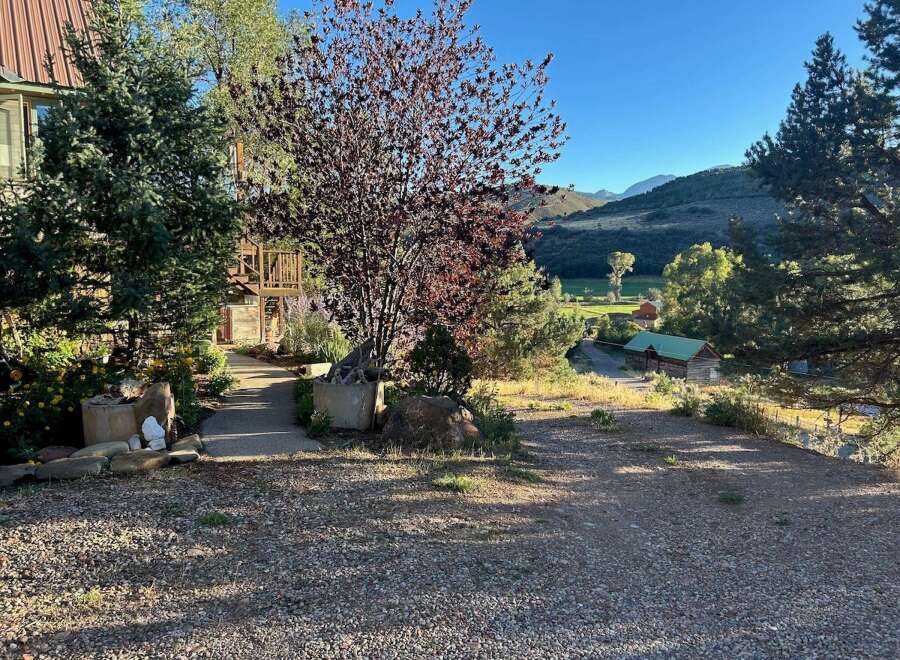 Discover this charming property nestled in a picturesque landscape, featuring a rustic log cabin with a green roof and a main house with a metal roof.