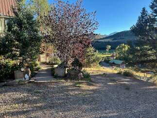 Discover this charming property nestled in a picturesque landscape, featuring a rustic log cabin with a green roof and a main house with a metal roof.
