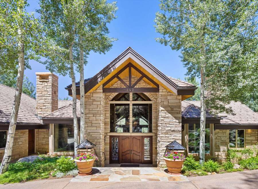 Experience luxury mountain living in this stunning stone-clad residence, featuring a grand double-door entrance framed by towering aspen trees.