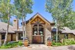 Experience luxury mountain living in this stunning stone-clad residence, featuring a grand double-door entrance framed by towering aspen trees.